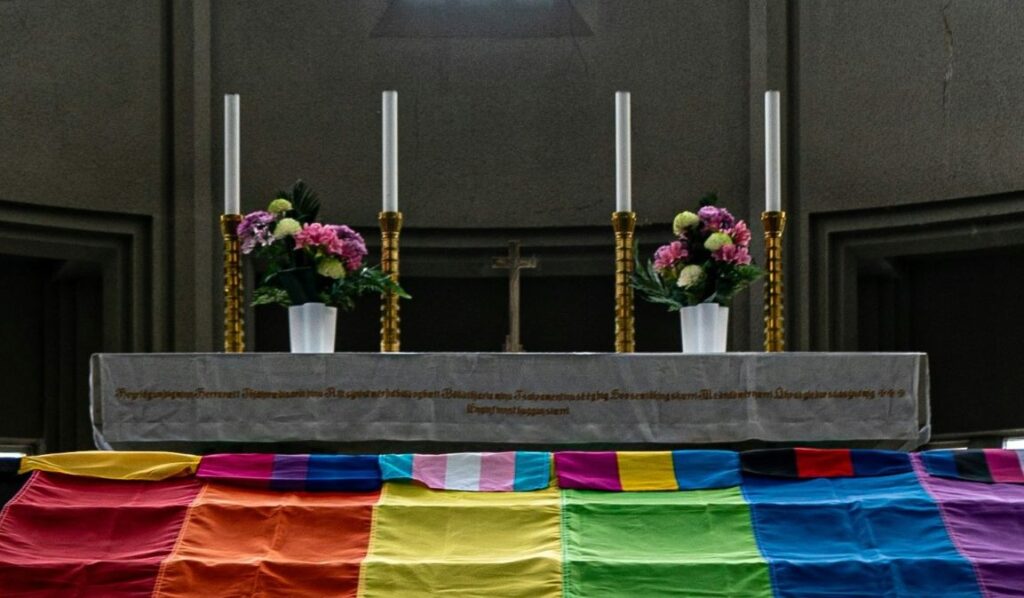 L’altar d’una església, amb una enorme bandera LGTBQ+ al davant.
