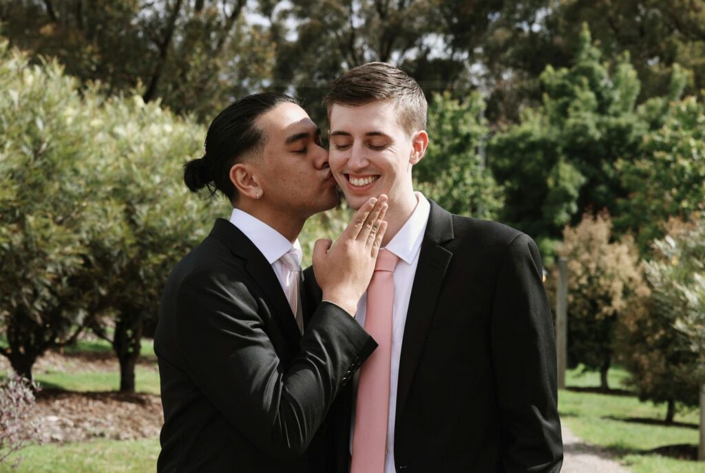 Dos homes joves vestits de nuvi, un donant un petó a l’altre.