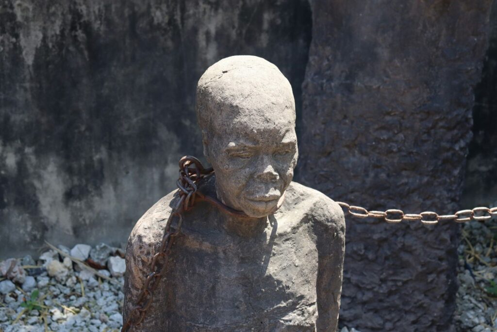 Estatua de una persona negra atada con una cadena en el cuello.